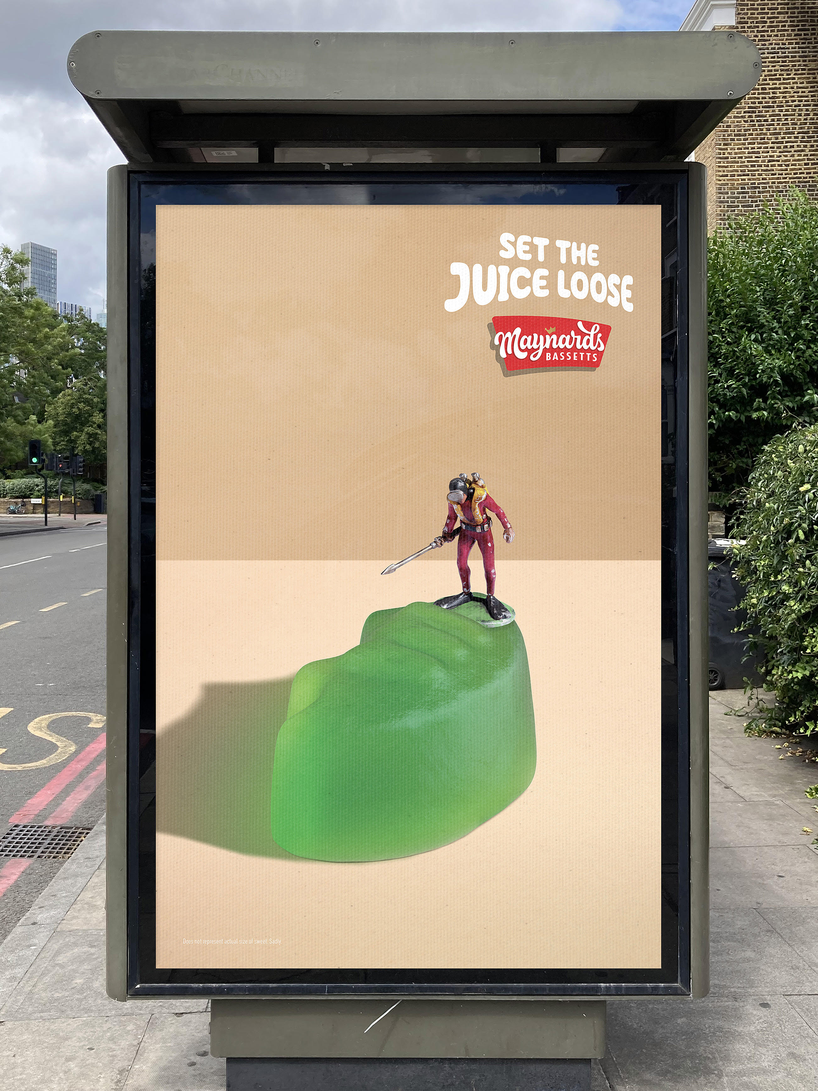 Poster showcasing a miniature model diver with a harpoon standing on top of a green winegum in the centre of the poster. Logo for Maynards Bassetts with endline saying set the juice loose in top right corner. 
The concept is to leave the viewer to imagine that when the harpoon pierces the skin of the sweet it would set the juice loose much like the explosion of flavour that happens in your mouth when eating Winegums.
